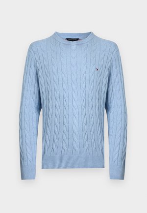 Világoskék kötött pulóver kerek nyakkivágással, bordázott mandzsettákkal és szegéllyel. Kis logó található a mellrészen. Puha anyagból készült.