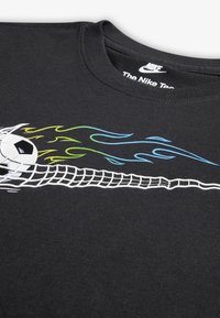 Μαύρο μπλουζάκι Nike με γραφικό ενός ποδοσφαιρικού μπάλας με στιλιζαρισμένες φλόγες σε πράσινο και μπλε χρώμα, και σχέδιο από δίχτυ ψαρέματος από κάτω.