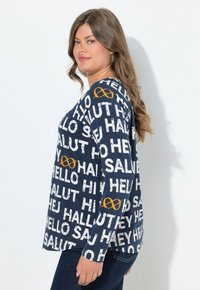 Námořnické tričko s dlouhým rukávem s bílými variantami textu "ahoj" a oranžovým nekonečným symbolem. Vyrobeno z jemné, hladké látky s volným střihem.