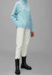 Jasnoniebieski sweter typu polo z dzianiny z prążkowanym wykończeniem, dopasowany z białymi spodniami typu tapered oraz czarnymi botkami na kostkę z grubą podeszwą.