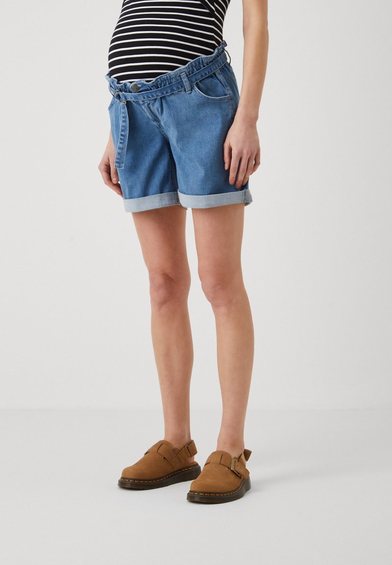 Jeansshorts med uppvikta fållar, med en åtsittande midja och framfickor. Bärs med bruna mocka sko utan snörning. Top med svart- och vitrandig mönster synlig.