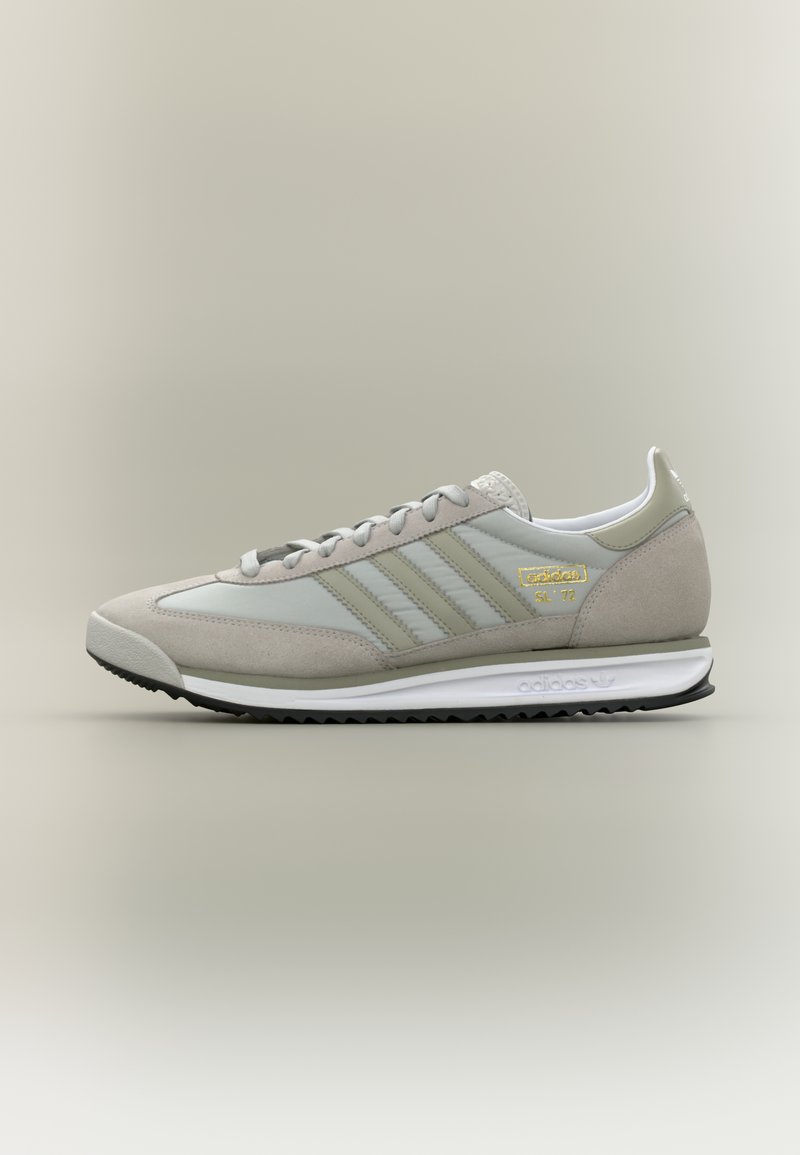 Αθλητικό παπούτσι ανοιχτού γκρι με συνδυασμό σουέντ και συνθετικού υλικού, με τρεις ρίγες, δέσιμο με κορδόνια στο μπροστινό μέρος και λευκή μεσαία σόλα.