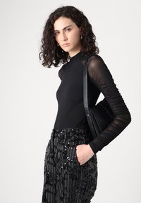 Body lungo nero a maniche lunghe con maniche trasparenti testurizzate, abbinato a pantaloni a righe neri e argento con paillettes, completato da una borsa nera.