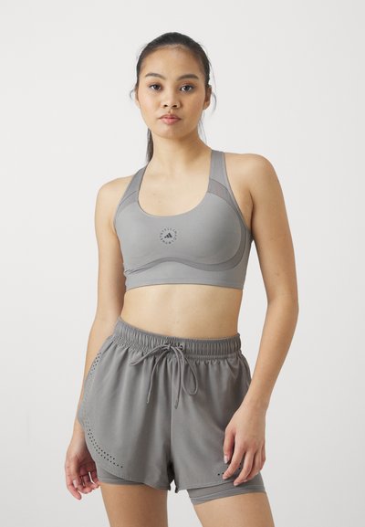 Sostén deportivo gris hecho de tela suave con un logotipo, acompañado de pantalones cortos grises a juego con cordón y detalles perforados.