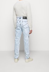 Vaqueros azul claro con efecto ácido, de talle alto, que presentan un parche de cuero en la parte trasera, bolsillos laterales y un ajuste relajado. Combinados con un suéter de punto color crema.