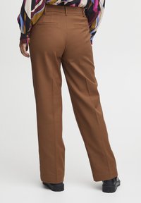 Pantaloni marroni su misura con design a gamba dritta, dotati di due tasche posteriori e una texture del tessuto liscia. Indossati con calzature nere.