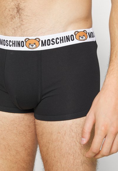 Boxer-briefs en coton noir avec une taille élastique blanche. La taille présente un logo d'ours brodé et "MOSCHINO" en lettres noires.
