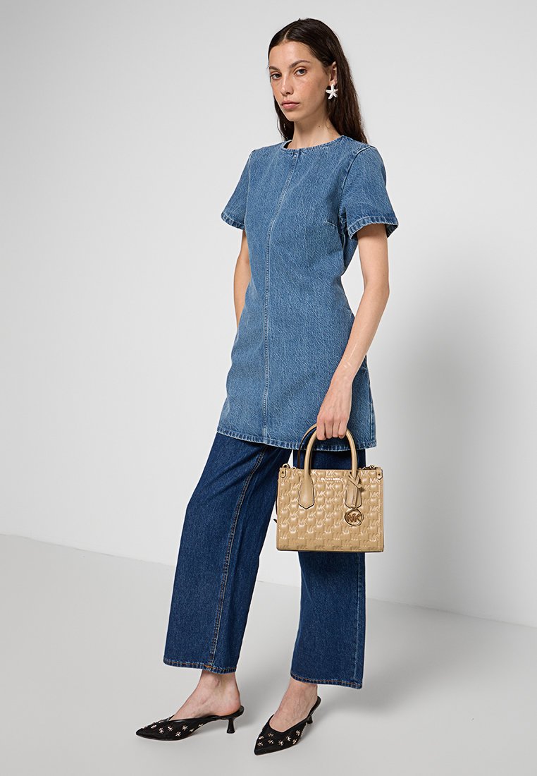 Robe en denim à manches courtes, coupe droite et couture sur le devant. Associée à un jean large et un sac à main à motifs beige. Chaussures noires à bout pointu.