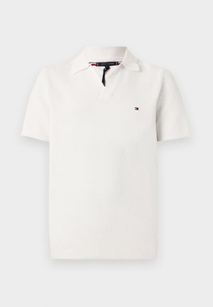 Polo shirt blanc à manches courtes en tissu tricoté texturé, avec un col en V, un col, et un petit logo sur la poitrine gauche.
