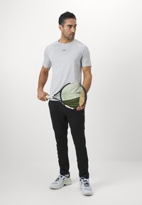Ljusgrå idrottströja med korta ärmar, tillsammans med svarta byxor. Vita och marinblå sneakers och ett tennisracket med ett grönt och svart rutmönster.