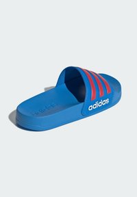 Niebieska sandałka na platformie z teksturowaną powierzchnią, z trzema czerwonymi paskami i białym logo "adidas" po boku. Smukły i minimalistyczny design.