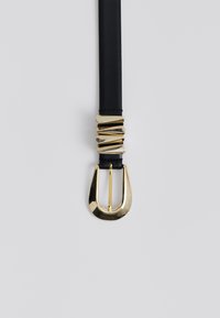 Cintura in pelle nera con grande fibbia dorata lucida e cinque accenti decorativi dorati irregolari vicino all'estremità della fibbia.