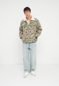 Floral patterned jacket with a cream faux fur collar, two front pockets, and relaxed fit. Worn with light blue jeans and white sneakers.