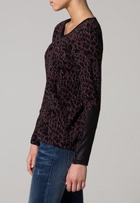 Camiseta de manga larga en burdeos oscuro con patrón de leopardo. Presenta un detalle de cuero negro en las mangas y un corte relajado.