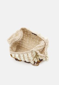 Světle béžová háčkovaná kabelka s kulatými flitrovými ozdobami a řetězovým držadlem ve vzoru želvoviny, zobrazená otevřená na bílém pozadí.