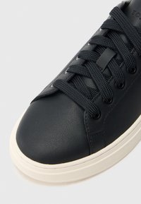 Mustast nahast toss ümmarguse varbaosaga, tekstuurse pinnaga, toonis paeltega ja kontrastse kreemja kummist tallaga. Puhas disain ja minimaalne detail.