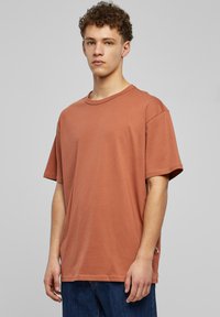 Základní oversized tričko v rezavé barvě vyrobené z bavlny, s kulatým výstřihem a krátkými rukávy, které má hladkou strukturu a minimální designové detaily.