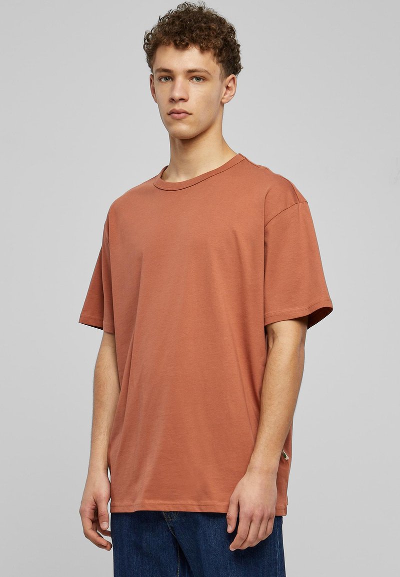 Základní oversized tričko v rezavé barvě vyrobené z bavlny, s kulatým výstřihem a krátkými rukávy, které má hladkou strukturu a minimální designové detaily.