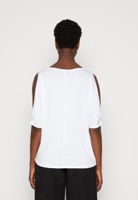 Witte, loszittende top met een bateauhals, korte opgerolde mouwen en een recht achterontwerp, gemaakt van zachte, lichte stof.