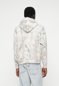 Camouflage hoodie in lichtgrijze tinten met een door de natuur geïnspireerd patroon. Voorzien van een capuchon met trekkoord en elastische manchetten, gemaakt van zachte stof.