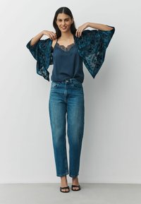 Navy satin camisole with lace trim, paired with high-waisted blue jeans and a sheer floral patterned kimono. Black slide sandals complete the look.