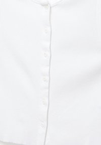 Chemise blanche à manches longues avec fermeture boutonnée sur le devant, avec de petits boutons blancs sur un fond uni.