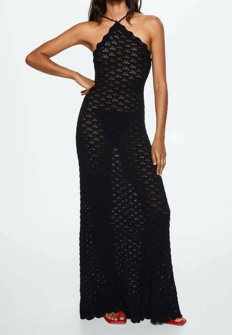 Femme portant une robe maxi noire en crochet sans manches à col halter et des sandales rouges à bout ouvert, debout avec une main sur la hanche.