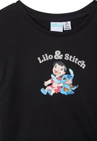 T-shirt nera in cotone con una grafica di Lilo e Stitch. Il design include colori vivaci e testo audace con una finitura scintillante.