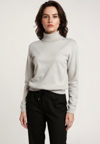 Lichtgrijze coltrui van zacht materiaal, met een ribbelstructuur bij de hals en lange mouwen, gecombineerd met zwarte broek met elastische taille.