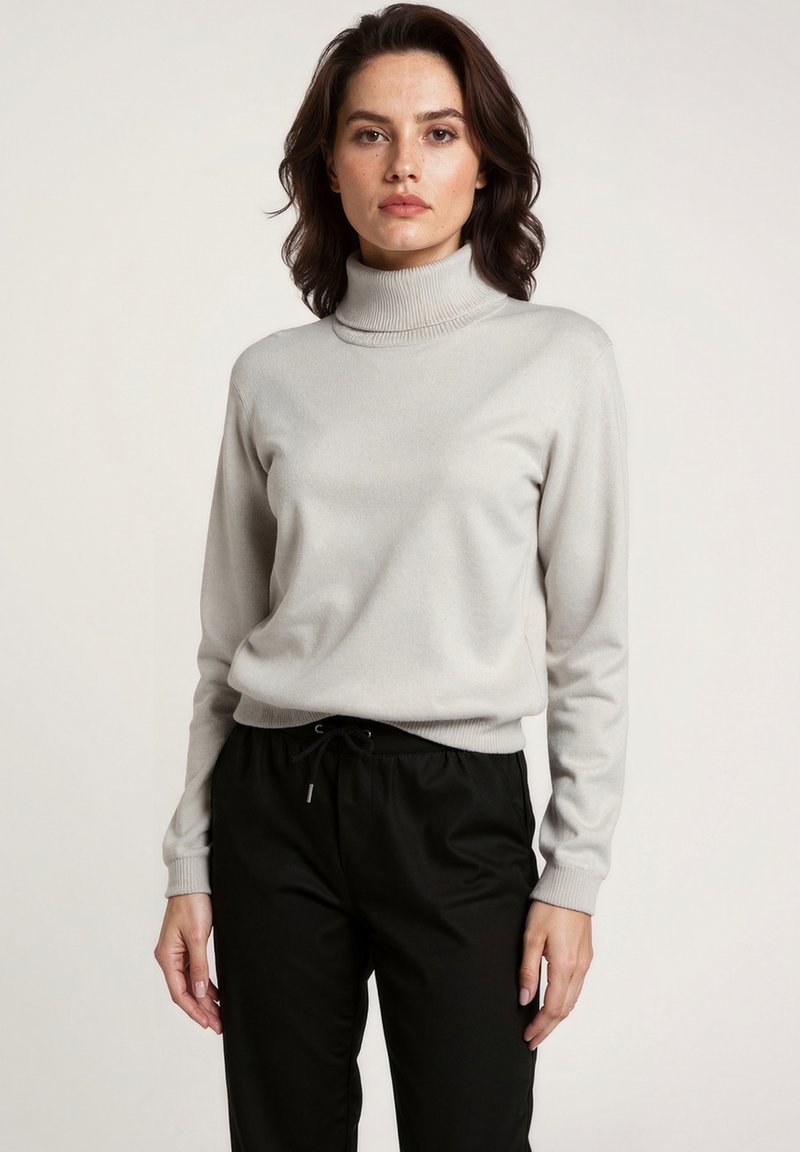 Lichtgrijze coltrui van zacht materiaal, met een ribbelstructuur bij de hals en lange mouwen, gecombineerd met zwarte broek met elastische taille.