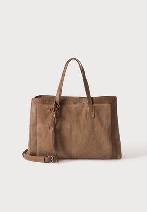 Sac cabas en daim et cuir marron avec doubles poignées, bandoulière détachable et détail pompon décoratif sur fond uni.