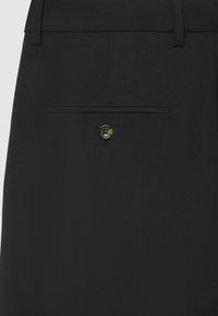 Pantaloni neri su misura con tasca posteriore orizzontale chiusa da un bottone rotondo, realizzati in tessuto liscio con una finitura fine.