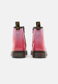 Różowe lakierowane botki na kostkę z czarnymi akcentami, zamkiem błyskawicznym i błyszczącą, fakturowaną podeszwą. Posiadają żółte pętelki do ściągania.