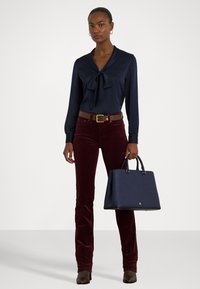 Marineblouse met strikdetail, bordeaux corduroy pantalon, bruine leren riem en marinehandtas met bovenhandvatten. Gevarieerde stoffen, getailleerd ontwerp.