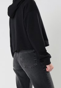 Hoodie negro corto con capucha, combinado con jeans de mezclilla gris oscuro de tiro alto, que cuentan con bolsillos traseros y un corte recto.