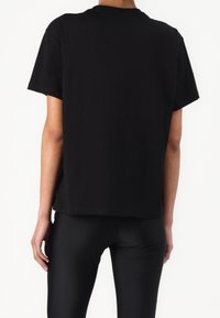 Black cotton t-shirt with short sleeves, a crew neck, and a relaxed fit. No visible graphics or patterns. Worn with black leggings.
