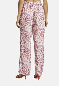 Pantalons à imprimé floral en tissu léger avec un fond rose pastel. Présentent des motifs de feuilles violettes et rouges, des jambes larges et une taille élastique.