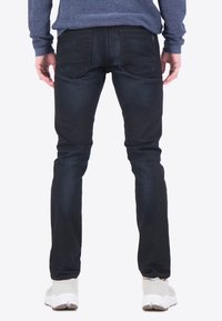 Jeans de mezclilla azul oscuro con un ajuste slim y un desvanecimiento sutil. Presenta dos bolsillos traseros y detalles de costura. Llevados con zapatillas de color claro.