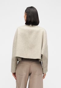 Krócony beżowy sweter z wełny z opuszczonymi ramionami, wykończonymi krawędziami i gładką fakturą. W zestawie z wysokim stanem beżowymi spodniami z kieszeniami.