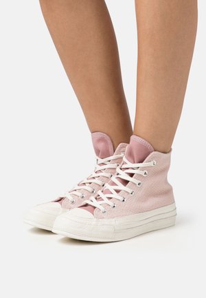 Lyserøde høje sneakers med tekstureret stof, hvid gummisål og kontrasterende hvide snørebånd. Har en buet tåhætte og ankelhøjde.