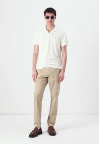 Krémszínű, rövid ujjú póló, bézs nadrág és barna loaferek. Slim fit, lapos gallérral és egy kis logóval a mellrészen.