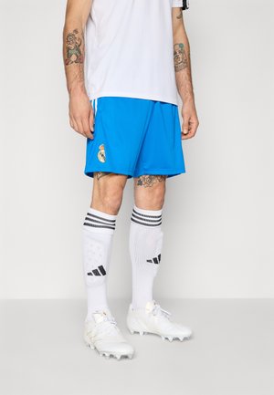 Plave atletske kratke hlače s logom Real Madrida, uparene s bijelim čarapama s crnim prugama i bijelim kopačkama. Lagana tkanina, ležeran kroj.