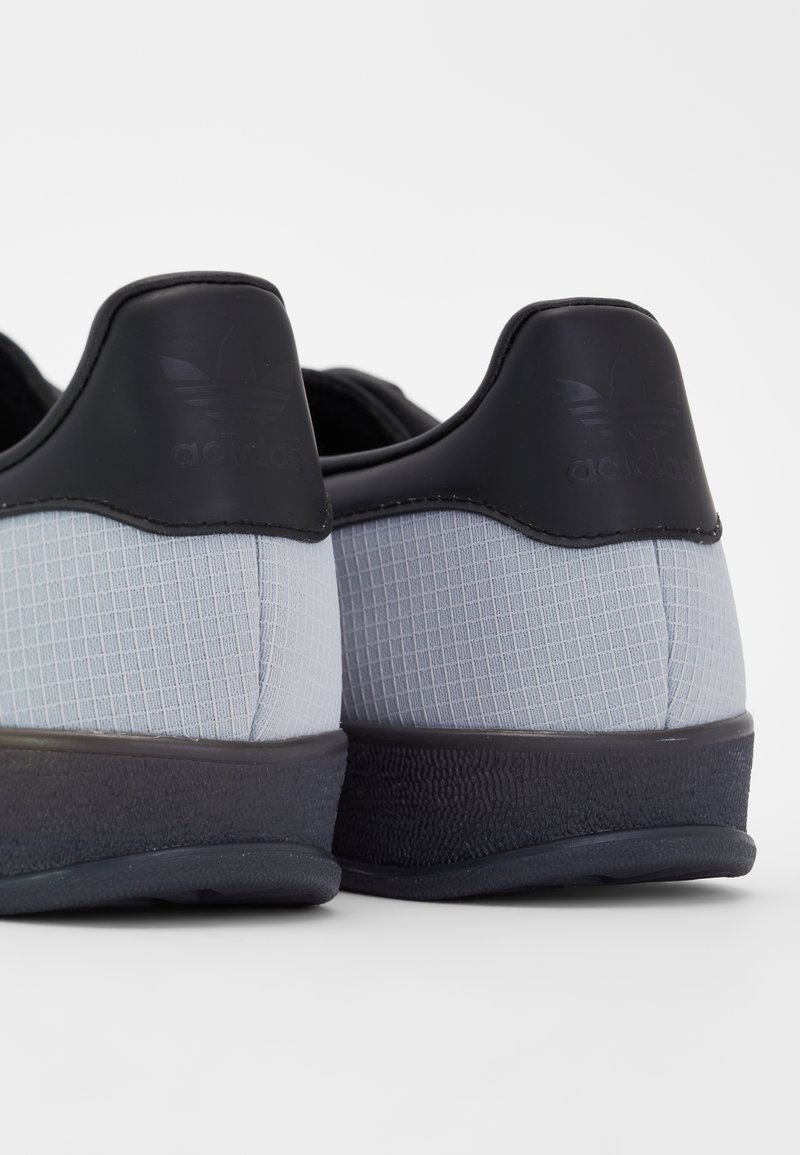 Graue und schwarze Sportschuhe mit einer strukturierten Oberseite, die ein Gittermuster aufweist und ein solides schwarzes Fersenpaneel hat. Gummisohle mit griffiger Textur.