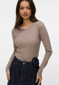 Langarm ribgebreide top in taupe, gecombineerd met een donkere denim rok met een stoffen roos als accent op de tailleband.