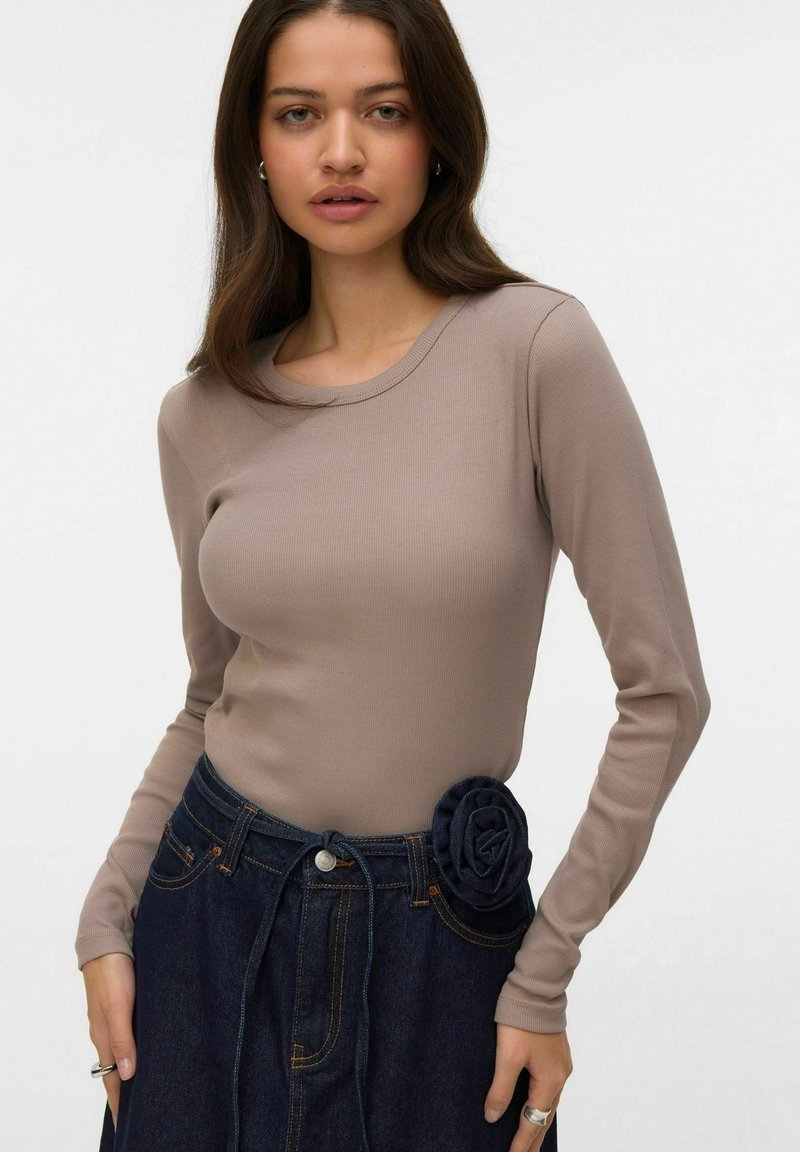 Langarm ribgebreide top in taupe, gecombineerd met een donkere denim rok met een stoffen roos als accent op de tailleband.