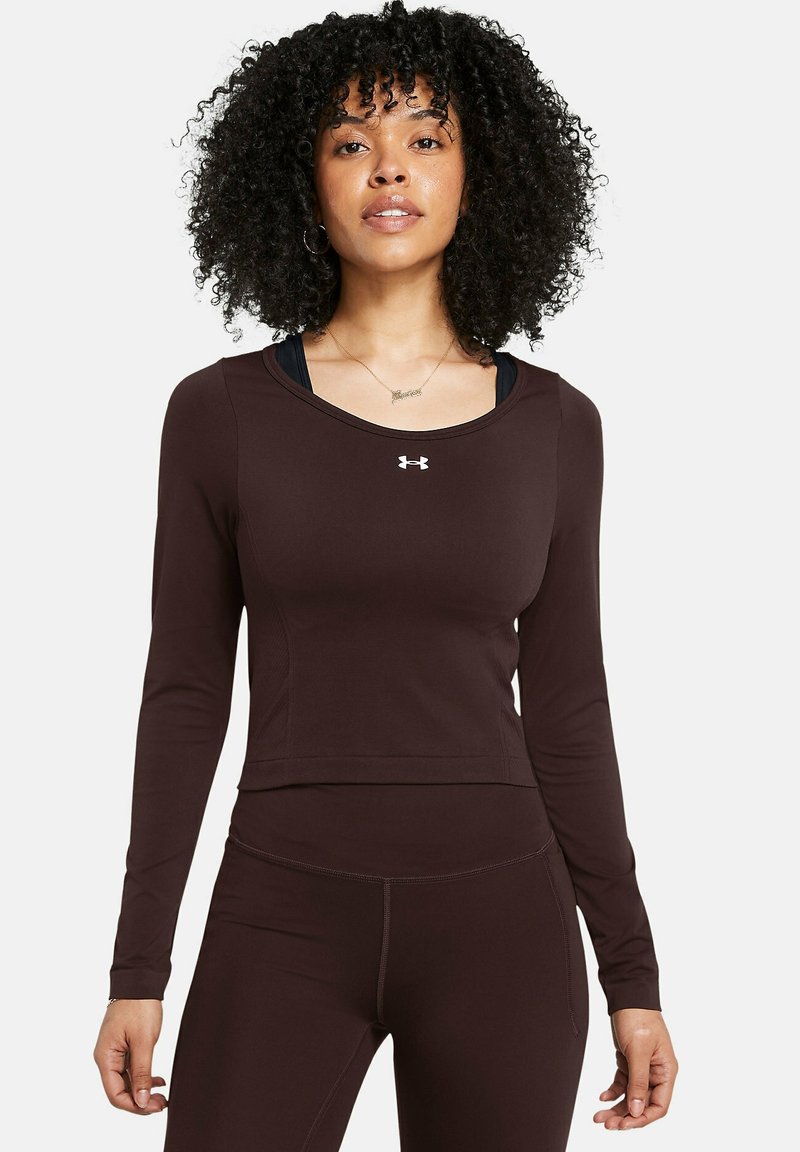 Brown long-sleeve athletic top with a scoop neckline and fitted design. Features an Under Armour logo on the chest. Smooth texture, lightweight material.
