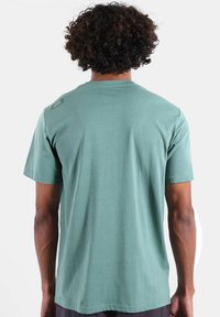 T-shirt vert menthe en tissu doux. Manches courtes et encolure ronde avec une petite étiquette logo sur l'épaule gauche. Texture lisse.