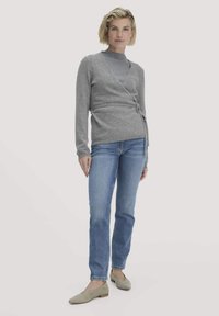 Grauer Wickelcardigan mit langen Ärmeln und einem Bindegürtel, kombiniert mit hellblauen Jeans und beigen Ballerinas. Glatte Textur und schlichtes Design.