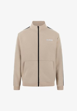 Beige tõmblukuga jakk, mis on valmistatud puuvilla segust. Omab musti külgtriibusid, kahte eesmist taskut ja kõrget kraed, millel on tikandiga logo.