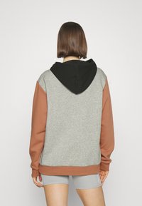 Mikina s kapucí v šedé barvě těla, hnědých rukávech a černé kapuci. Vyrobena z měkké látky, s uvolněným střihem a žebrovanými lemy na rukávech.